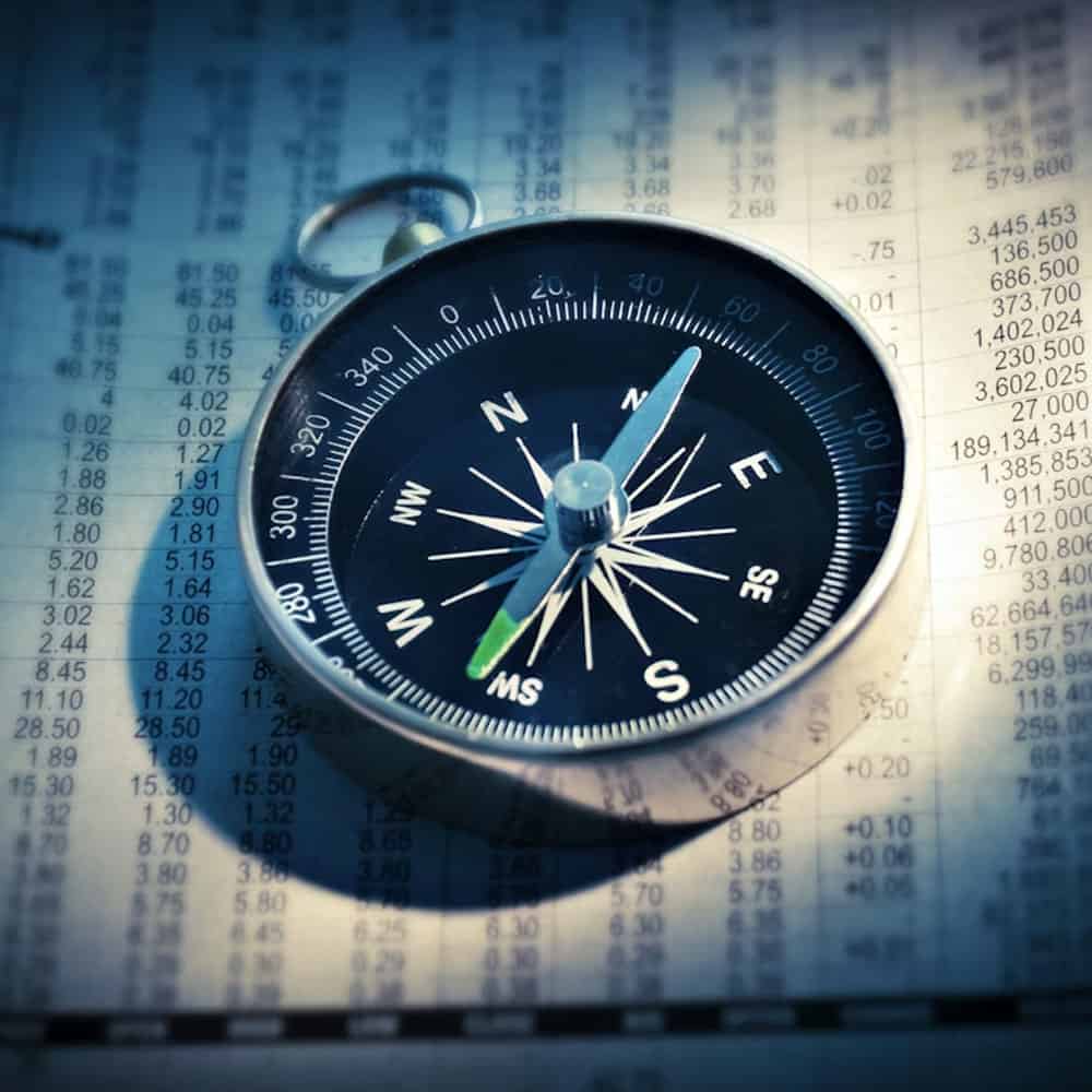 Boussole posée sur un tableau financier avec chiffres et données.